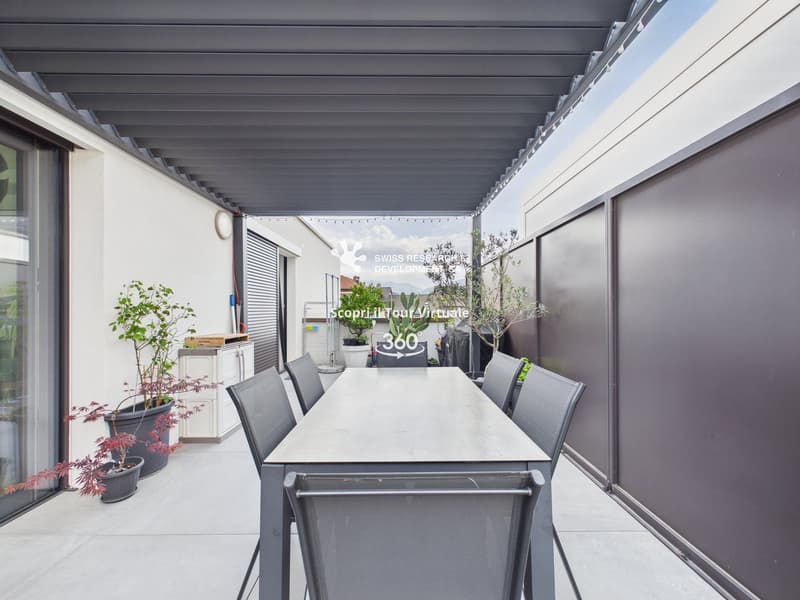 Outdoor dining area with a table and chairs, covered by a pergola, surrounded by potted plants, and a glass wall
