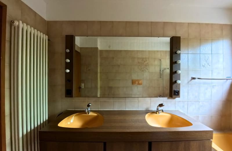 Bathroom with double sink, mirror, tiled walls, bathtub, radiator