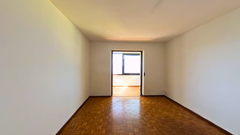 Empty room with wooden floor, white walls, and a window leading to another room