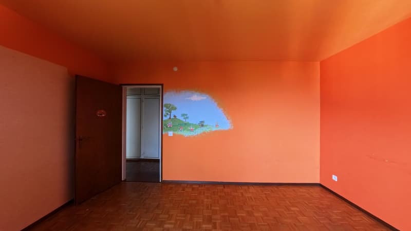 Empty room with wooden floor, orange walls, open door, and a mural on the wall