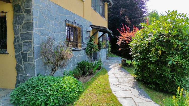 Stone and yellow wall, black metal railings, lamp, plants, pathway, garden