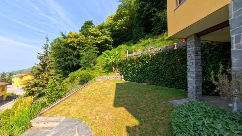 green lawn, stone wall, plants, trees, yellow house, view of the mountains