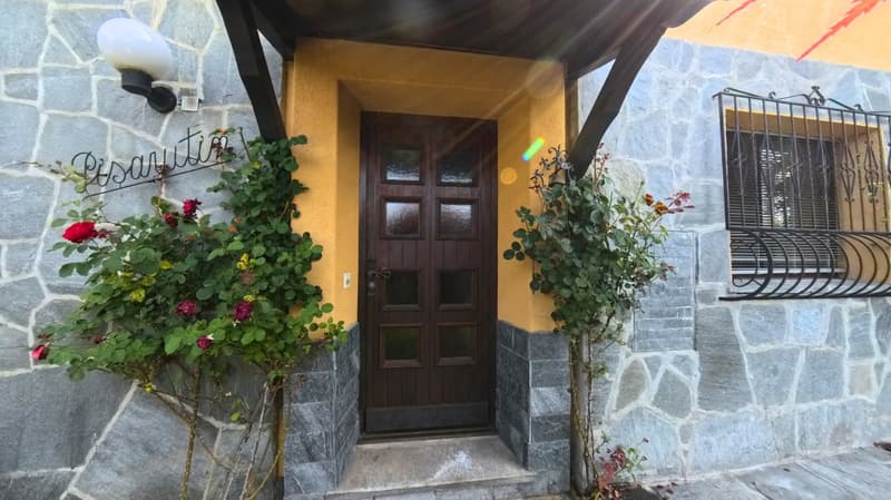 Stone wall, wooden door, yellow wall, black railing, plants with red flowers