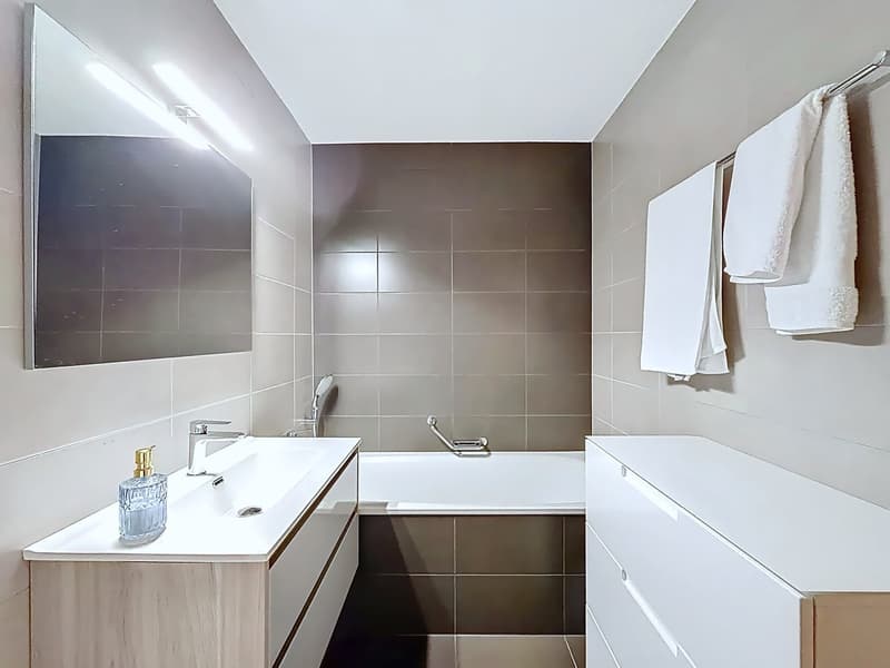 Bathroom with bathtub, sink, mirror, and towel rack with towels