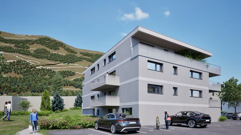 A modern, multi-story apartment building with a flat roof, large windows, and a parking area in front. The building is surrounded by greenery and hills in the background.