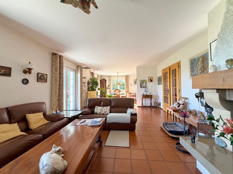 Cozy living room with brown leather sofas, wooden coffee table, tiled floor, fireplace, decorative items, wall lamps, glass windows, and framed pictures.