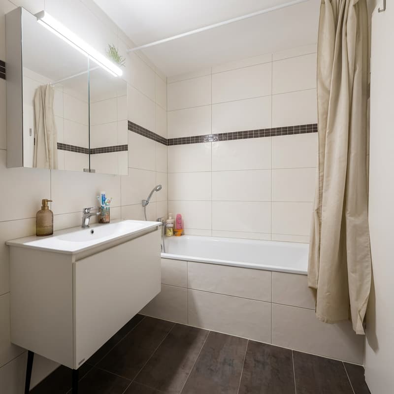 modern bathroom with a bathtub, a white vanity, a toilet, mirror, and tiled walls