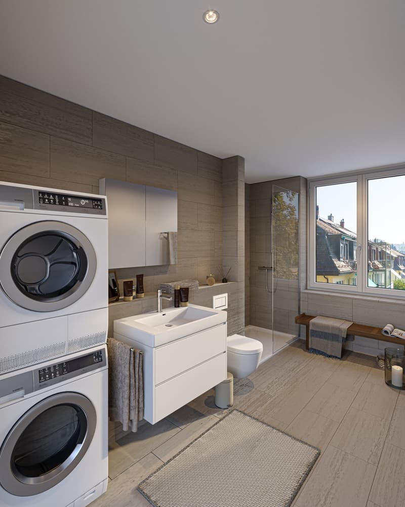 Modern bathroom with washer and dryer, vanity sink, toilet, and glass shower enclosure. The room has a minimalist, neutral color scheme with wood-paneled walls and large windows providing natural light.