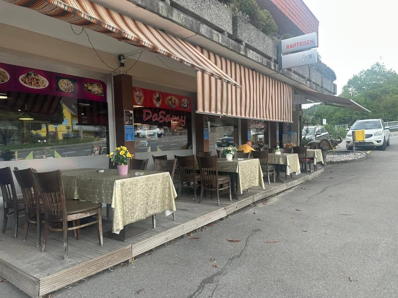Restaurant exterior with awnings, outdoor dining tables, chairs, flower vases, and a parking area