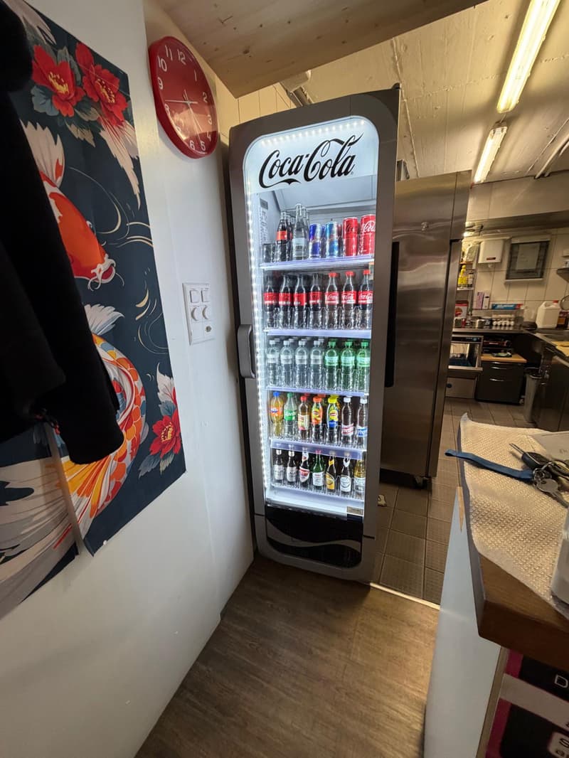 Coca-Cola vending machine, wall with floral wallpaper, clock, wooden floor, stainless steel appliances