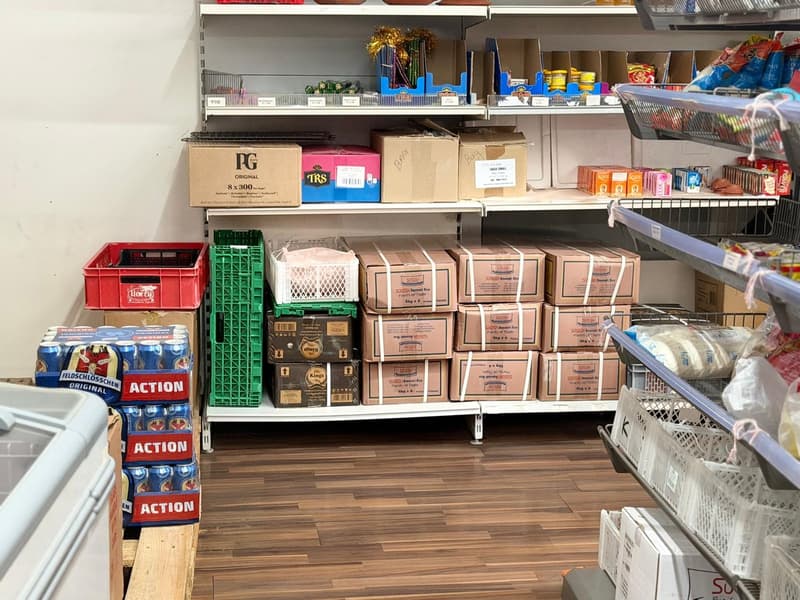 A room with shelves filled with various boxes and products, a wooden floor, and a white wall.