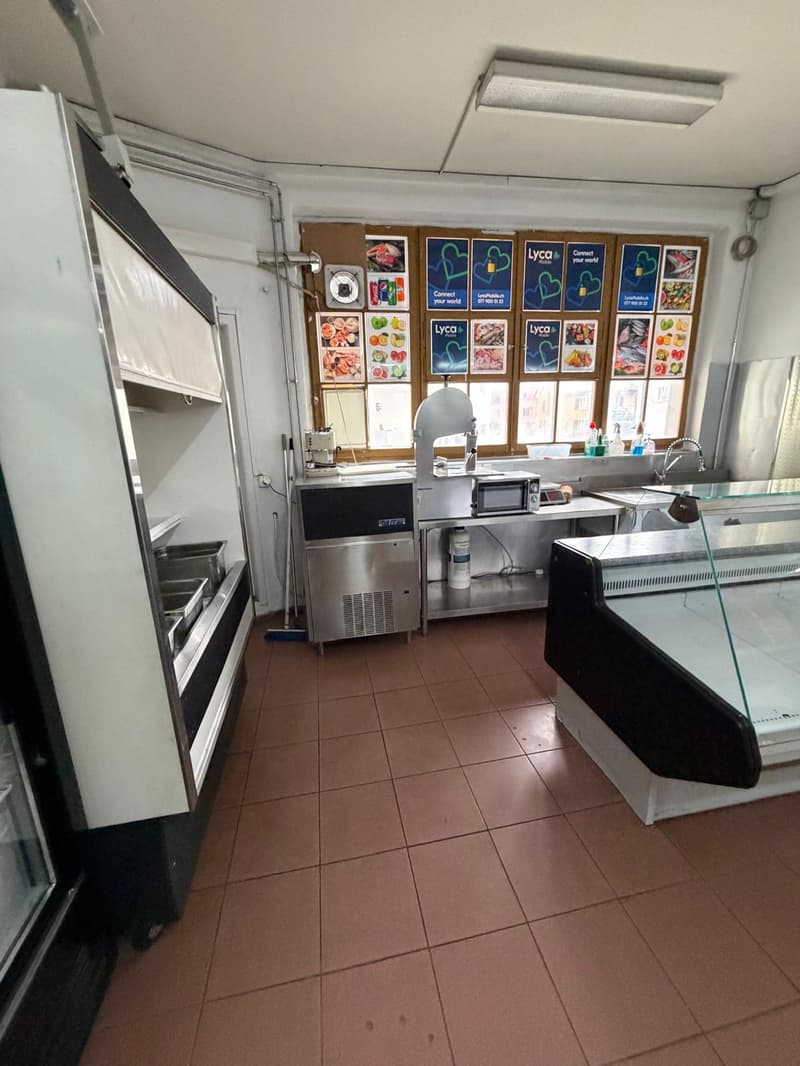 Commercial kitchen with stainless steel appliances, tiled floor, large windows, and a display case.