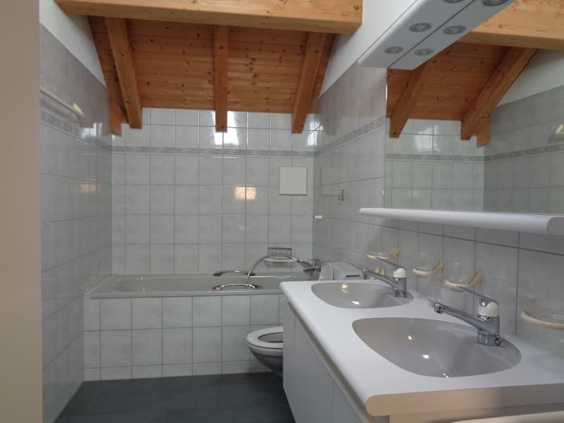 white tiled walls, wooden ceiling, bathtub with showerhead, sink with faucets, toilet, shelf