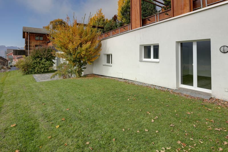 white building with glass sliding doors, large well-kept grassy area, decorative tree, balcony on the top floor