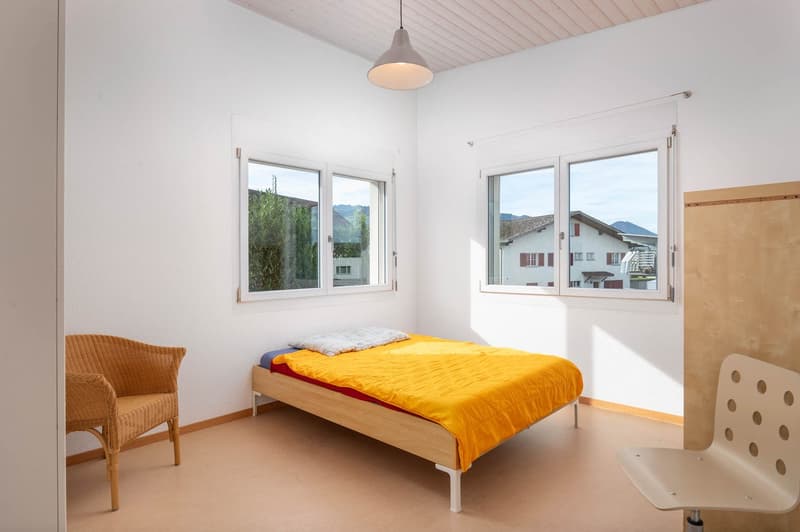 Spacious room, bed, chair, white walls, wooden floor, large windows, outdoor view