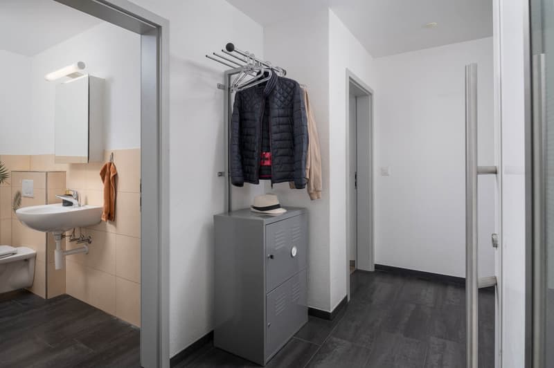 Bathroom with sink, mirror, toilet, tiled wall, and storage cabinet.