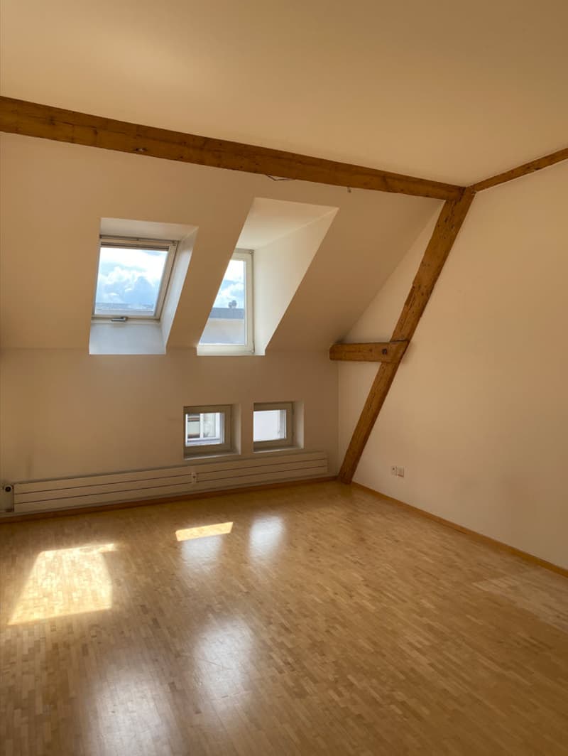 Attic room with wooden beams, hardwood floor, large windows, and a small balcony or terrace