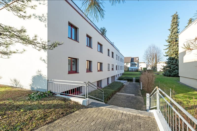3-story apartment building, white exterior, multiple windows, red frames, brick paved walkway, entrance stairs
