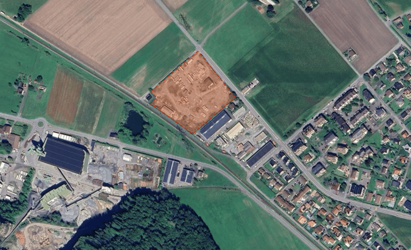 Large residential property in development with surrounding roads, nearby fields, industrial buildings, residential areas, trees, and water bodies