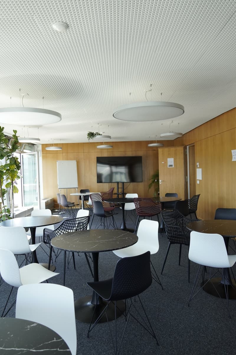 modern office space with round tables, chairs, TV, whiteboard, wooden walls, plants