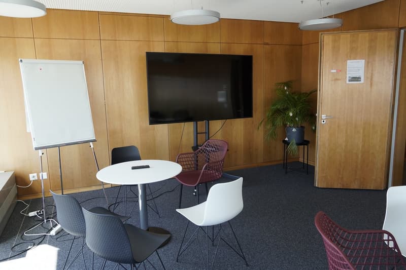 modern office room with wooden walls, a whiteboard, a flat screen TV, a round table, and several chairs