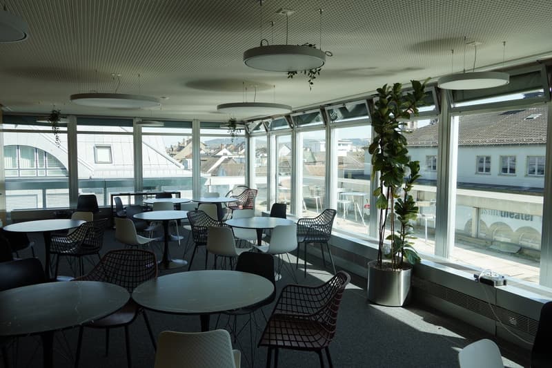 modern office with round tables, chairs, large windows, plants, ceiling lamps