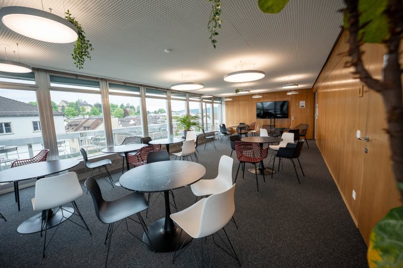 modern office space with round tables, chairs, large windows, plants, TV