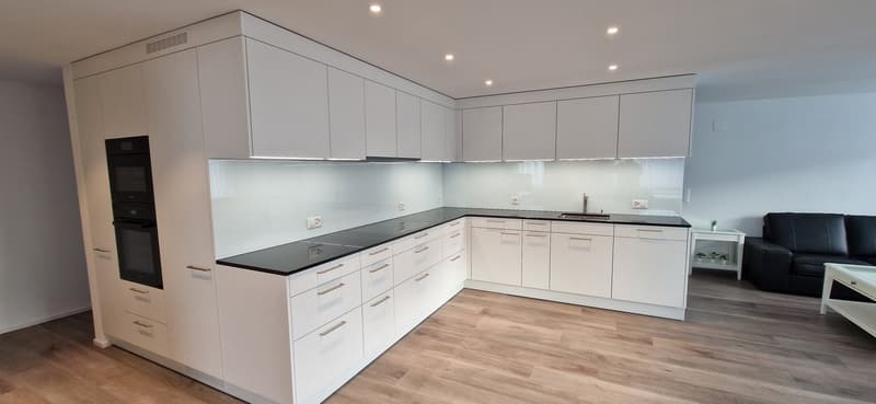 Modern, open-concept kitchen with white cabinets, black countertops, built-in appliances including a dishwasher, and hardwood flooring