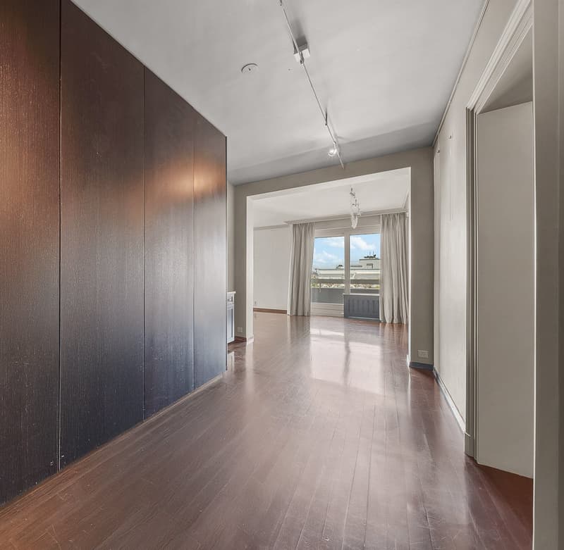 Large open room with hardwood floors, dark brown wooden wall panels, and a window with curtains providing a view to the outside.