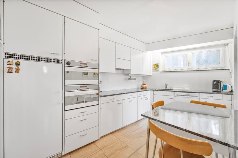 Modern kitchen with white cabinetry, granite countertops, wooden floor, dishwasher, washing machine, and double oven.