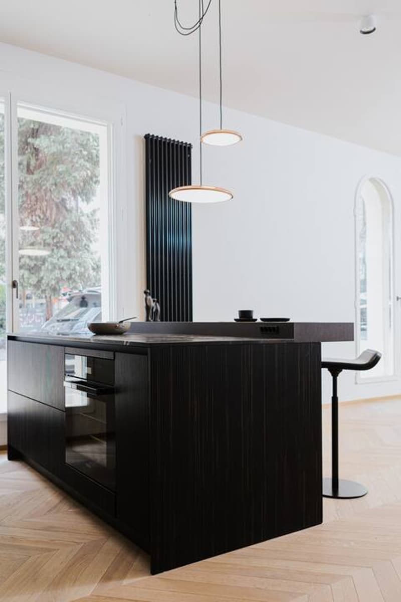 Modern kitchen with black cabinetry, wooden countertop, and pendant lighting. The kitchen island has a built-in dishwasher.