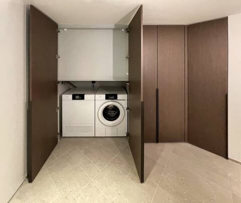 Spacious utility room with built-in washing machine and dishwasher, ample storage space with dark brown cabinets, and tiled flooring.