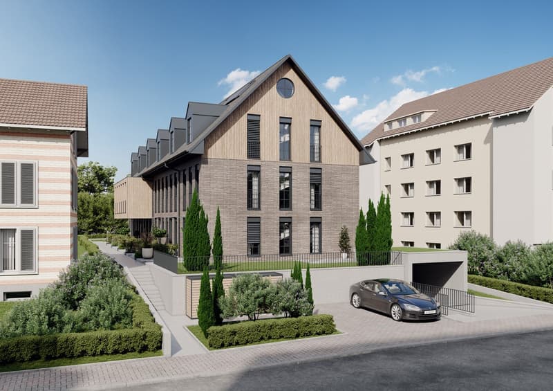3-story apartment building with a modern, wooden-clad facade, large windows, and a circular window at the top. The building is surrounded by landscaping, including cypress trees and other greenery. A Tesla electric vehicle is parked in the driveway in fro