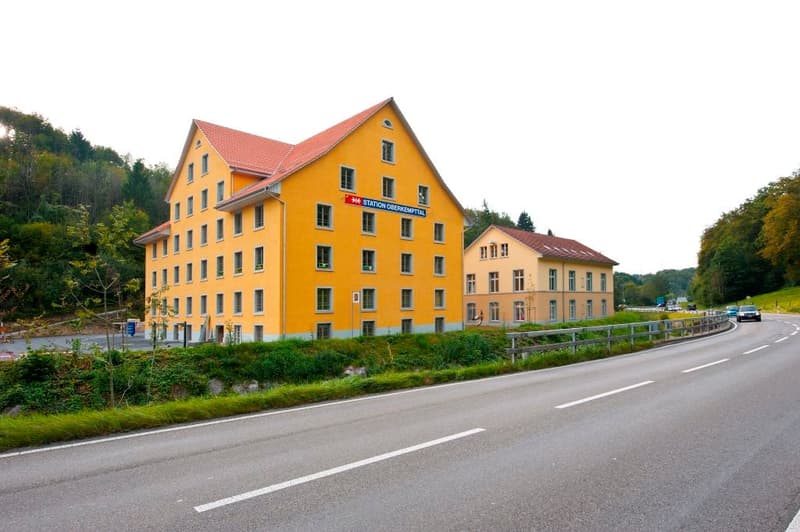 5-story yellow building with red roof, located next to a road with a parking area visible