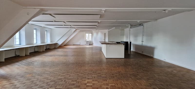 Large room, hardwood floor, three windows, central desk with white cabinetry