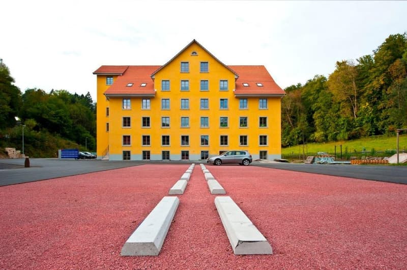 3 story yellow building, red roof, multiple windows, red driveway, cars parked