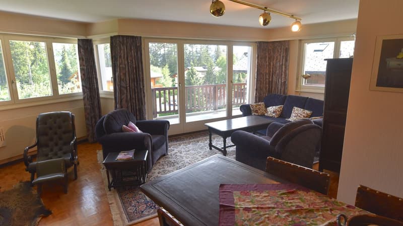 Spacious living room with large windows overlooking a balcony, hardwood floors, dark sofas, coffee table, and decorative pillows