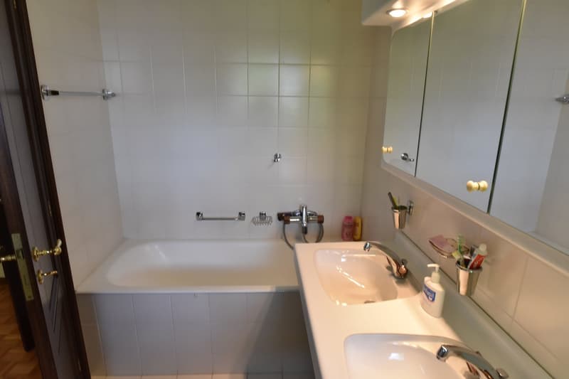 Tiled bathroom with a bathtub, sink, and vanity mirror. There is a towel rack and some personal care items visible.