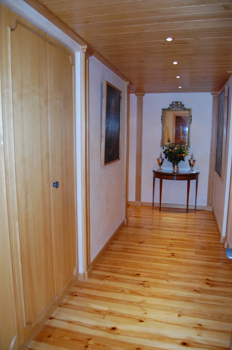 Wooden ceiling, wooden floors, white walls, ornate framed mirror, table with floral arrangement