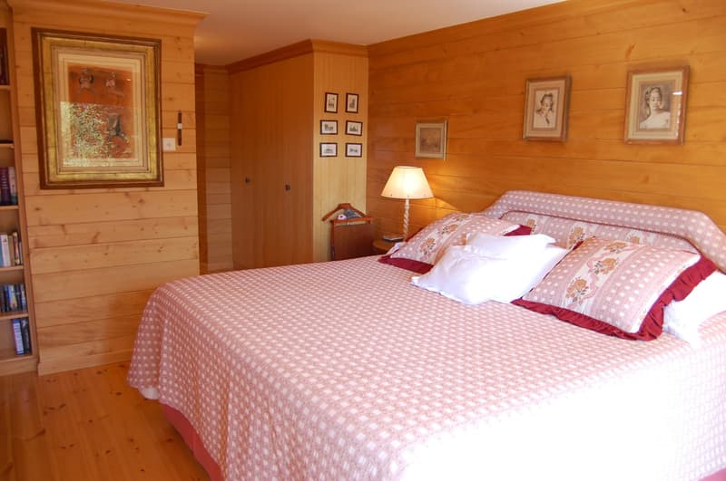 Cozy wooden bedroom with a large bed, patterned bedding, framed artwork on the walls, and a lamp on the nightstand.