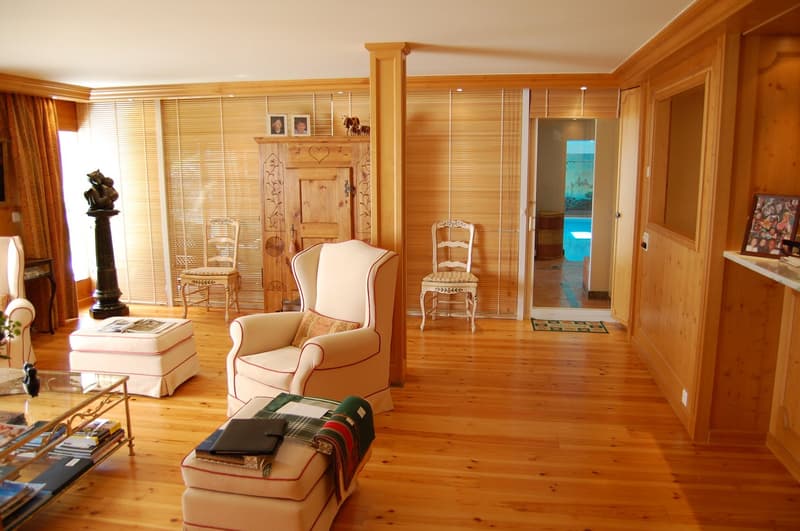 Spacious living room with wooden walls and floors, large windows, armchairs, wooden furniture, and a fireplace