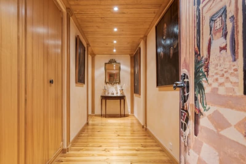 Wooden paneled hallway with a fireplace, artwork on the walls, and a wooden floor.