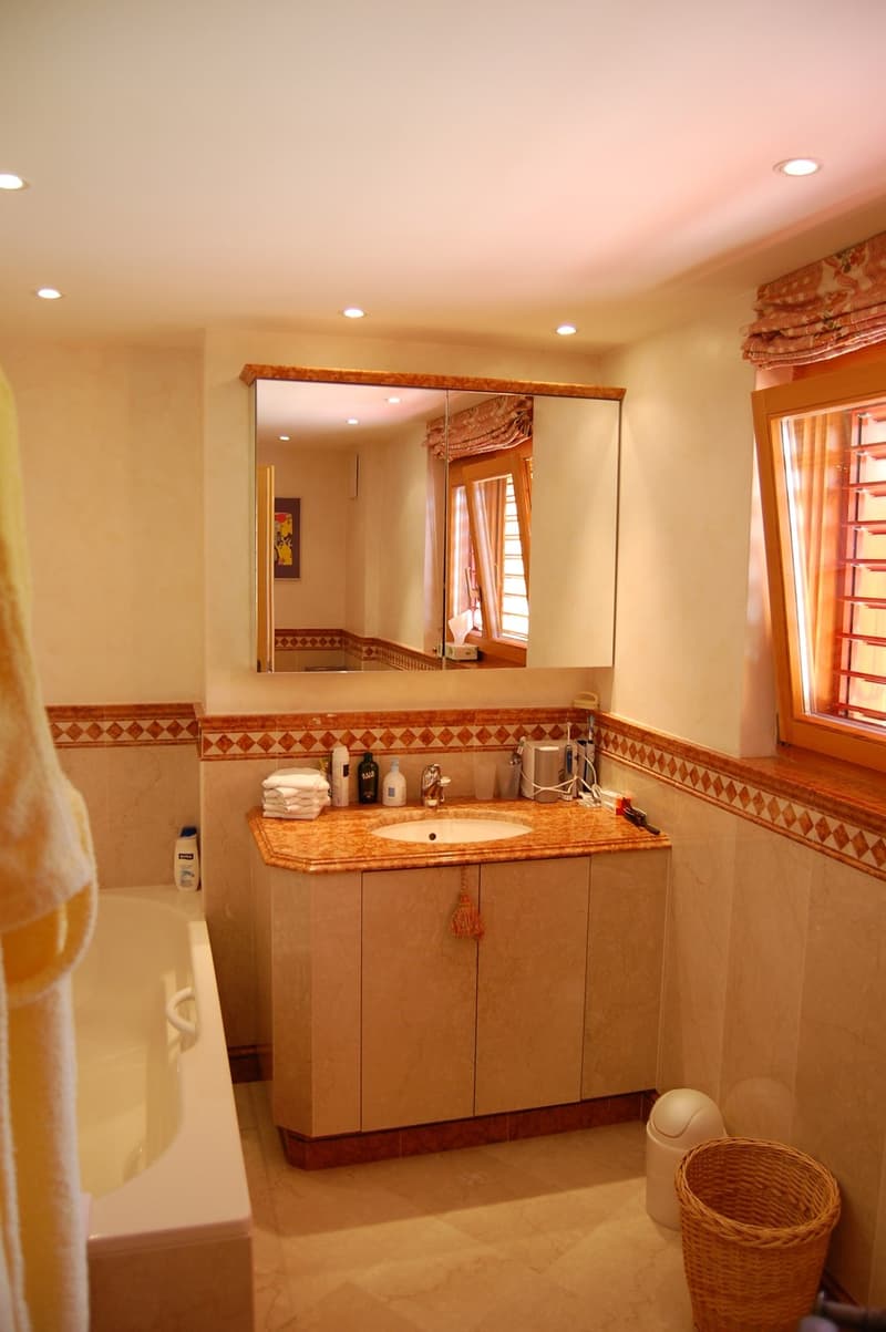 Spacious bathroom with a vanity sink, large mirror, and decorative tile work. The room also features a wicker basket, suggesting the presence of a private washing machine.
