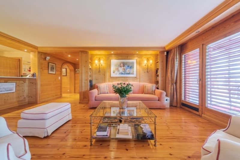 Spacious living room with wooden walls and floors, large windows, pink sofa, glass coffee table, and a fireplace