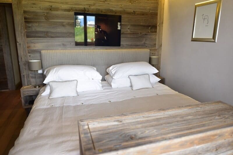 Rustic wooden walls, large bed with white bedding, nightstands, and a flat-screen TV mounted on the wall.