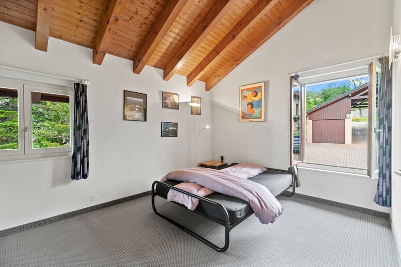 Spacious bedroom with wooden beamed ceiling, large windows, artwork on the walls, and a metal framed bed with pink bedding