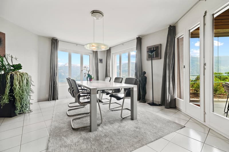 Spacious dining room with large windows offering a scenic view, modern dining table and chairs, pendant lighting fixture, potted plant, and artwork on the wall.