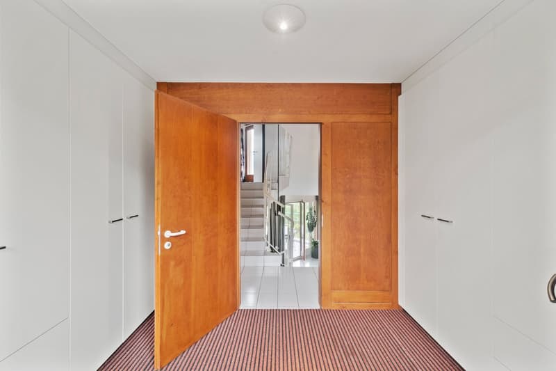Wooden entrance door, white walls, wooden trim, view of stairs and hallway through the open door