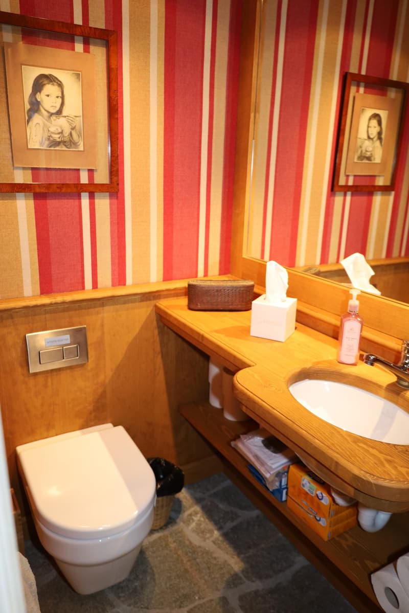 Bathroom with wooden vanity, toilet, and framed portraits on the striped red and yellow walls