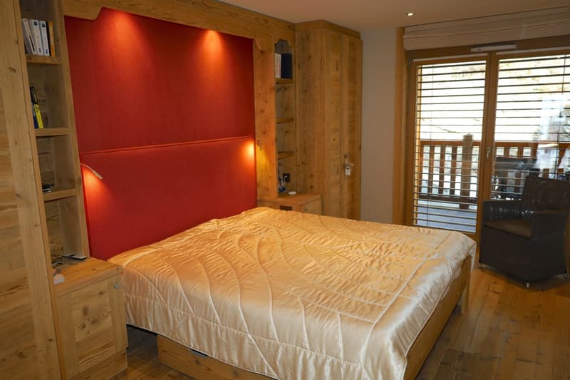 Wooden bedroom with double bed, red headboard, wooden shelves, sliding door with balcony access
